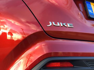 Een zonsondergang die reflecteert op de achterkant van een Nissan Juke, met de modelnaam zichtbaar.
