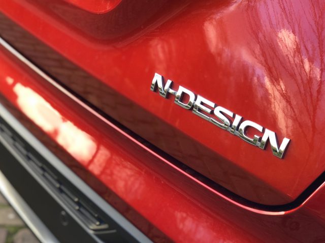 Close-up van de rode carrosserie van een Nissan Juke met een 'n-design'-badge.