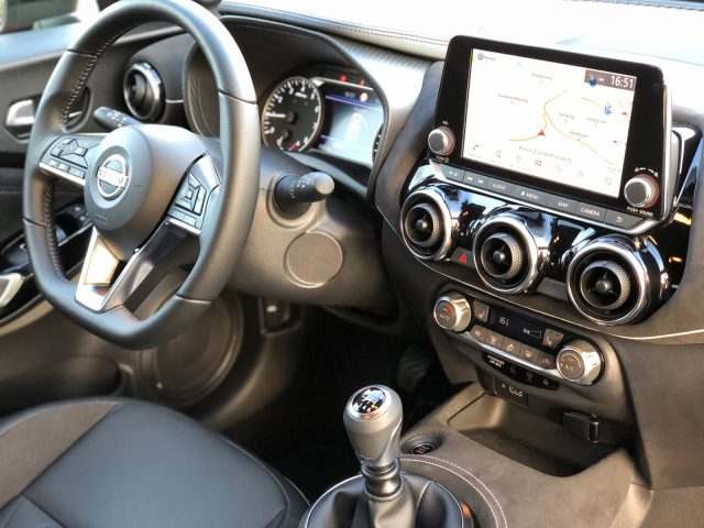 Interieur van een moderne Nissan Juke met het stuur, het dashboard, de handgeschakelde versnellingsbak en het infotainmentsysteem met een kaartnavigatiescherm.