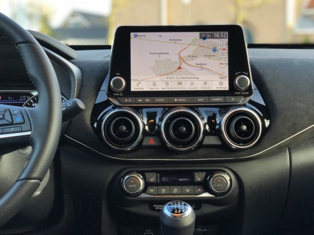 Het dashboard van een Nissan Juke met een infotainmentsysteem met een navigatiekaart op het scherm, ventilatieopeningen en klimaatregeling.