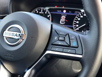 Stuur van een Nissan Juke met cruise control-knoppen en een digitaal dashboard zichtbaar op de achtergrond.