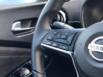 Stuur en bedieningselementen van een Nissan Juke-voertuig met zicht op het interieur van de bestuurdersdeur.