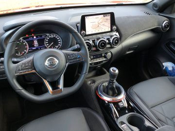 Binnenaanzicht van een Nissan Juke met een digitaal dashboard, centraal touchscreen-display en handgeschakelde versnellingsbak.
