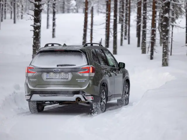 Subaru Forester rijdt door een besneeuwd boslandschap.