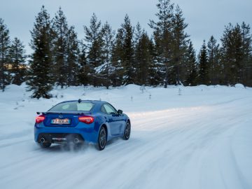 Blauwe Subaru-sportwagen die op een besneeuwde weg rijdt te midden van een winterlandschap.