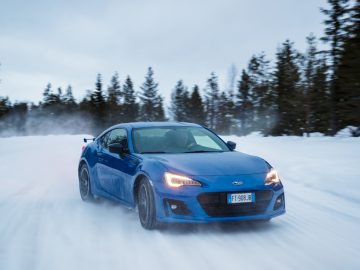 Blauwe Subaru-sportwagen in beweging op een besneeuwde weg.