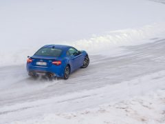 Een blauwe Subaru BRZ die over een besneeuwde weg rijdt, met daarachter opspattend sneeuw.
