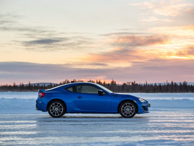 Een blauwe Subaru-sportcoupé geparkeerd op een bevroren meer in de schemering.