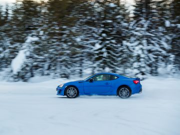 Een blauwe Subaru-sportwagen in beweging op een besneeuwde bosweg.