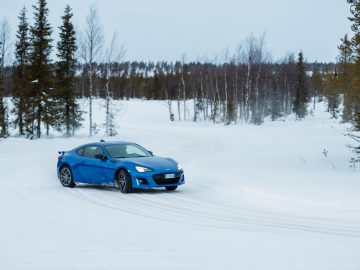 Blauwe Subaru-sportwagen die op een besneeuwde weg drijft in een winterboslandschap.