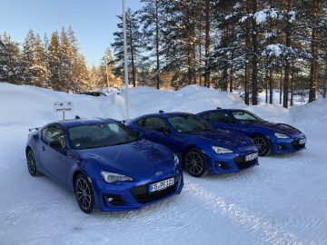 Drie blauwe Subaru Foresters geparkeerd op besneeuwde grond met bomen op de achtergrond.
