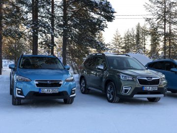 Twee Subaru Forester-auto's geparkeerd op een met sneeuw bedekt terrein met bomen op de achtergrond.