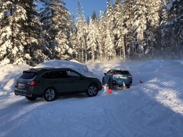 Auto's, waaronder een Subaru Forester, geparkeerd op een besneeuwd pad met omringende met sneeuw bedekte bomen en één voertuig gedeeltelijk bedekt met sneeuw.
