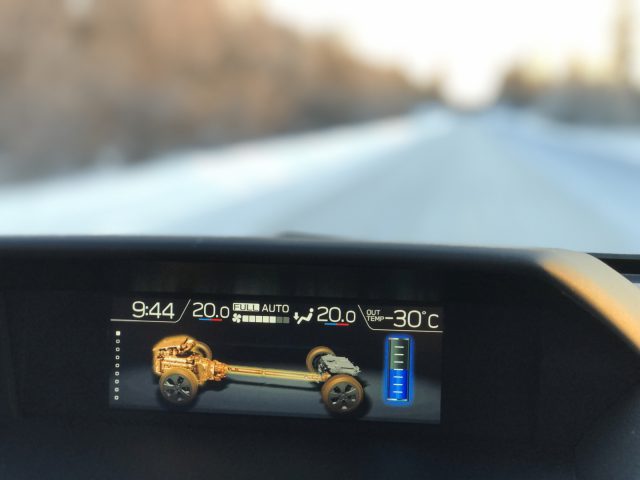Het dashboarddisplay van een Subaru Forester toont voertuiginformatie met een wazige winterweg op de achtergrond.