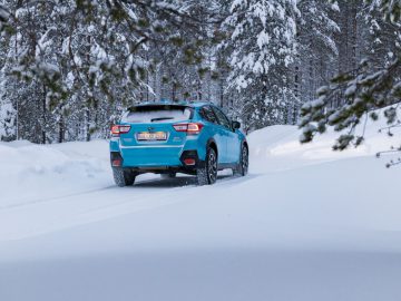 Een Subaru XV e-Boxer rijdt op een besneeuwde weg midden in een winters boslandschap.