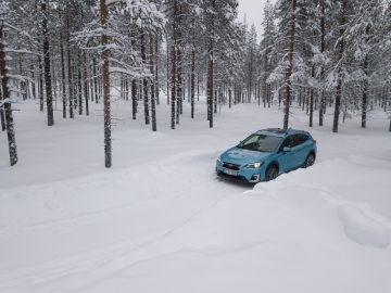 Blauwe Subaru XV e-Boxer rijdt op een besneeuwd bospad.