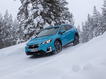 Blauwe Subaru XV e-Boxer SUV rijdt door een besneeuwde bosweg tijdens een sneeuwval.