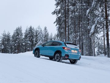 Een blauwe Subaru XV e-Boxer geparkeerd op een besneeuwde weg in een bos in de winter.