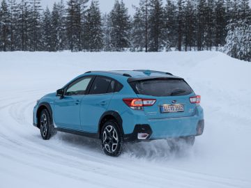 Blauwe Subaru XV e-Boxer rijdt op een besneeuwde weg met een bos op de achtergrond.