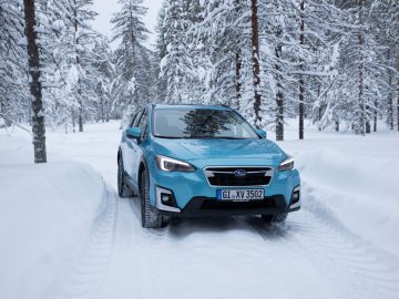 Een blauwe Subaru XV e-Boxer die over een besneeuwde weg rijdt, omringd door winterse bosbomen.