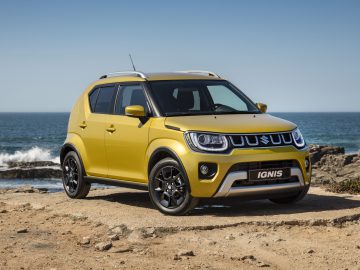 Gele Suzuki Ignis geparkeerd aan de kust op een zonnige dag.