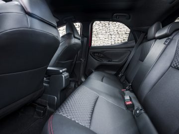 Binnenaanzicht van de achterbank van een Toyota Yaris met zwarte bekleding en een stenen muur zichtbaar door het raam.