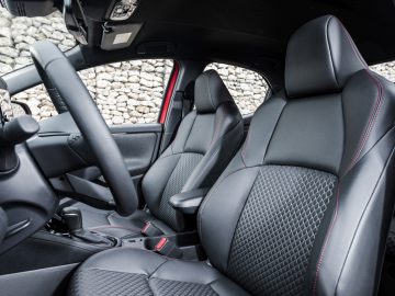 Binnenaanzicht van een moderne Toyota Yaris met de voorstoelen en het dashboard met rode stiksels op de bekleding.