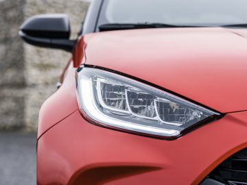 Close-up van de koplamp en het frontontwerp van een Toyota Yaris rode auto.
