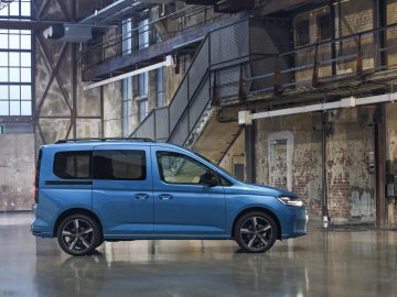 Blauwe Volkswagen Caddy geparkeerd in een industrieel pakhuis met rustieke achtergrond.