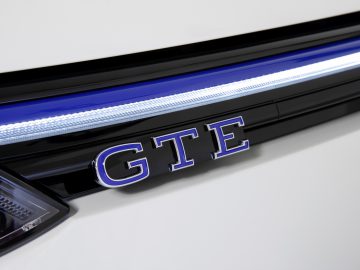 Close-up van het sierstuk van een Volkswagen Golf GTI met het "GTI"-embleem met een blauwe accentlijn.
