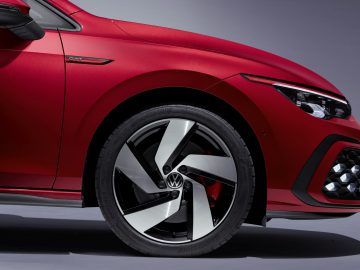 Close-up van het voorwiel en spatbord van een rode Volkswagen Golf GTI met een zichtbaar Volkswagen-logo op de velg.