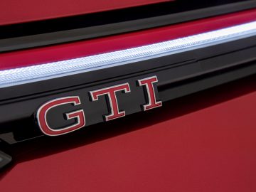 Close-up van een Volkswagen GTI-badge op de grille van een rood voertuig.