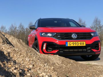 Rode Volkswagen T-Roc R SUV geparkeerd aan de kant van de weg met een helderblauwe lucht op de achtergrond.
