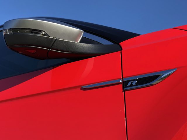 Rood sportwagendetail met zijspiegel, deurgreep en een badge die een krachtig Volkswagen T-Roc R-model aangeeft.