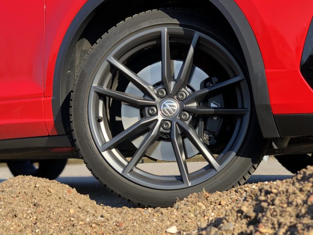 Rode Volkswagen T-Roc R met een zwarte lichtmetalen velg geparkeerd op een asfaltoppervlak naast een grindgebied.