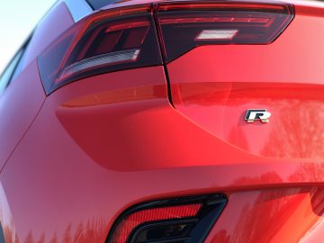 Close-up van de achterkant van een rode Volkswagen T-Roc R met een "R"-badge en een opvallend ontwerp van de achterlichten.