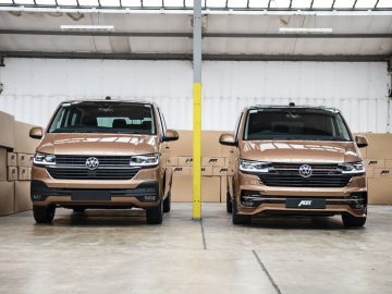 Twee Volkswagen Transporter-busjes geparkeerd in een magazijn met kartonnen dozen op de achtergrond.
