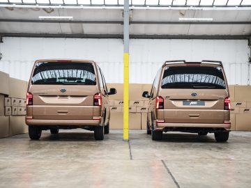 Twee identieke bruine Volkswagen Transporter-busjes stonden rug aan rug geparkeerd in een pakhuis omringd door kartonnen dozen.