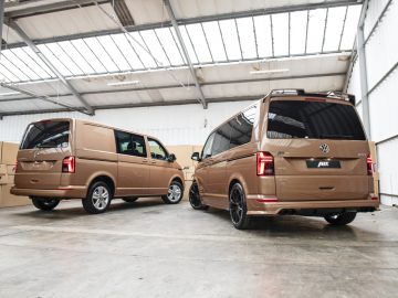 Twee Volkswagen Transporter-busjes geparkeerd in een magazijn, één met de achterdeur open.