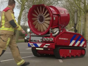 Brandweerlieden lopen naast een Blusrobot uitgerust met een grote ventilator.