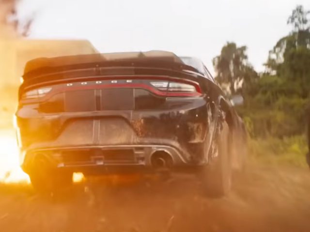 Een auto bedekt met stof uit Fast & Furious 9 maakt een snelle bocht op een onverharde weg met stof en zonlicht op de achtergrond.