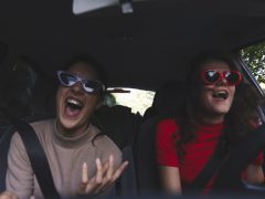 Twee vrouwen met een zonnebril die vrolijk lachen in een auto.