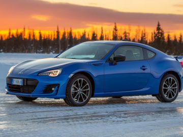 Blauwe Subaru-sportcoupé geparkeerd op een bevroren landschap bij zonsondergang.