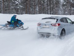 Een Subaru Impreza e-Boxer en een sneeuwscooter die zij aan zij over een besneeuwde weg reizen.