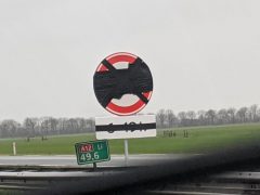 Een onleesbaar verkeersbord met een zwarte x eroverheen geschilderd, gezien vanuit een voertuig, geeft een snelheidslimiet aan van 100 kilometer per uur.