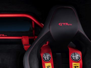 Zwarte sportautostoel met rode stiksels en Giulia GTA-logo, met rode racegordels met logogespen.