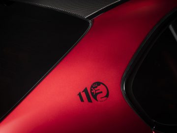 Close-up van een rode sportwagen met het nummer "110" en een steigerend paardenlogo op de carrosserie, met het opschrift "Giulia GTA".