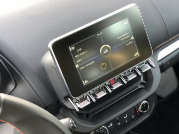 Scherm van het infotainmentsysteem met radiozender en klimaatregeling op het dashboard van een auto, waarbij de snelheid wordt weergegeven als 100 km/u.