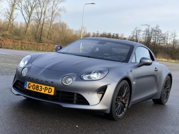 Matgrijze alpine sportwagen die overdag op een asfaltoppervlak geparkeerd staat en snelheden tot 100 km/u kan bereiken.