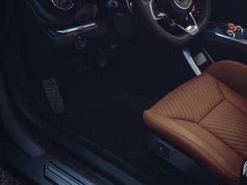 Luxe auto-interieur met leren stoel, modern dashboard en Alpine A110-logo op de deurdrempel.